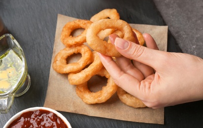 Woman eating fried onion rings with sauce at table