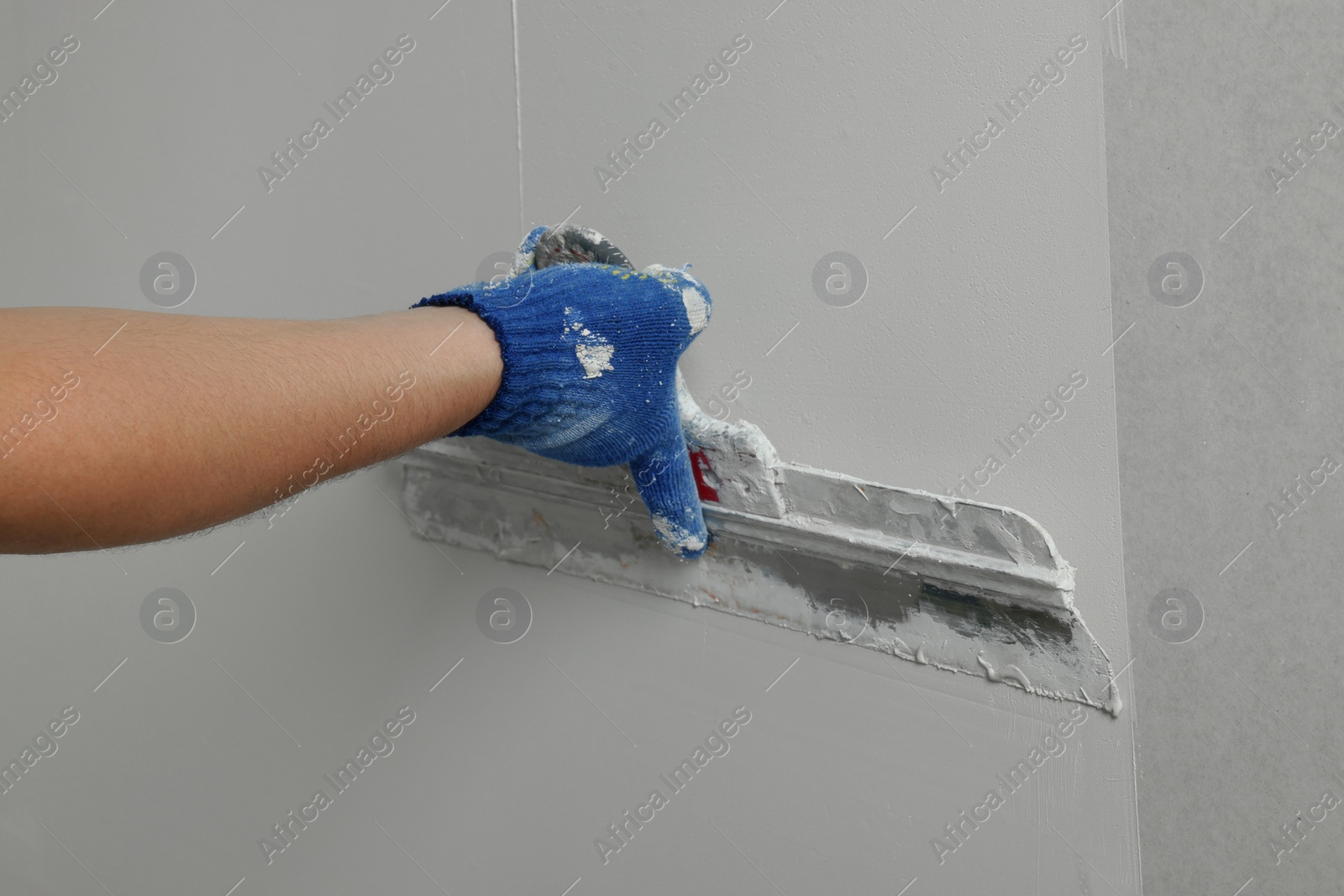 Photo of Professional worker plastering wall with putty knife, closeup