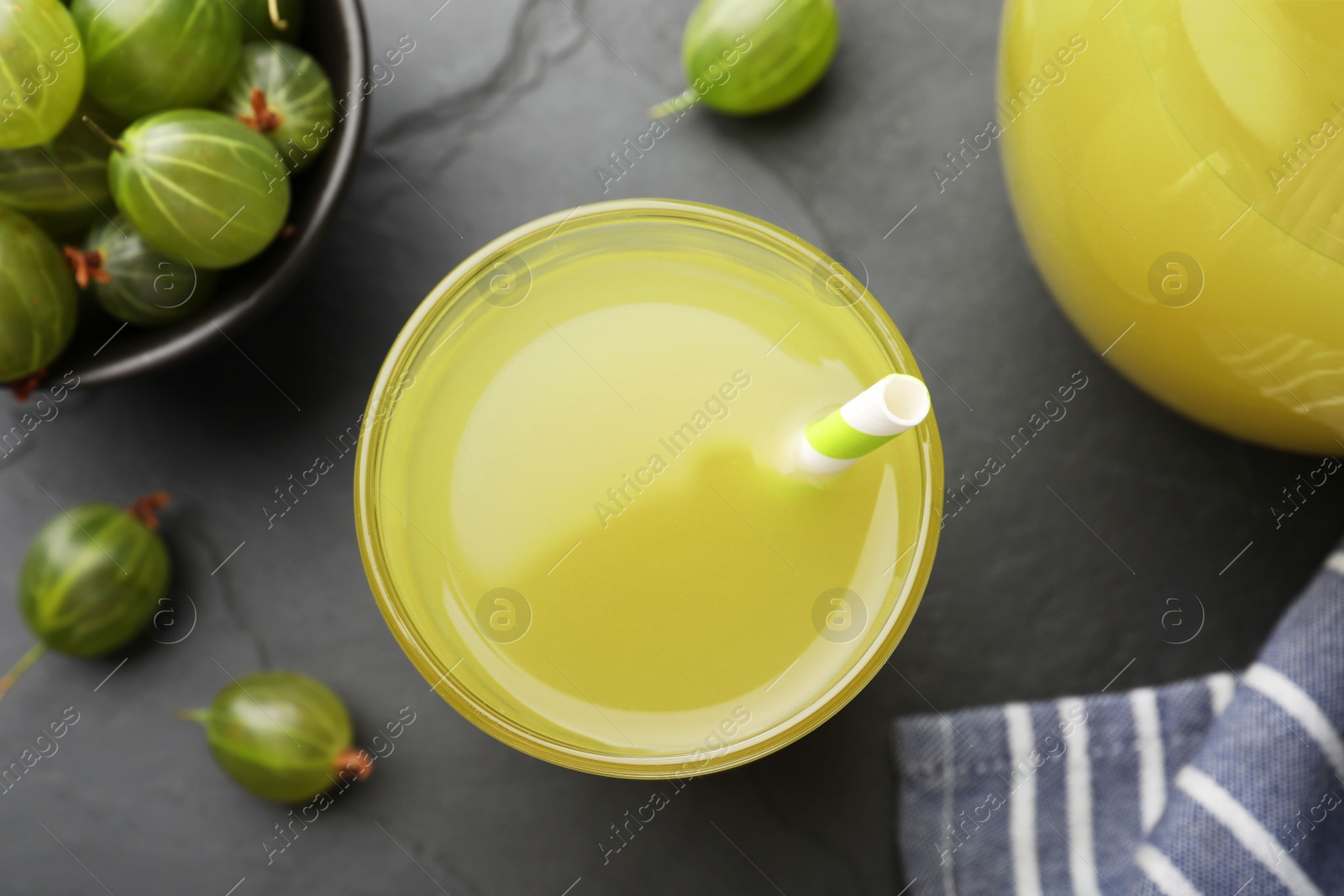 Photo of Tasty gooseberry juice in glass on black table, flat lay