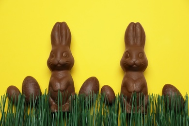 Chocolate Easter bunnies and eggs with green grass on yellow background