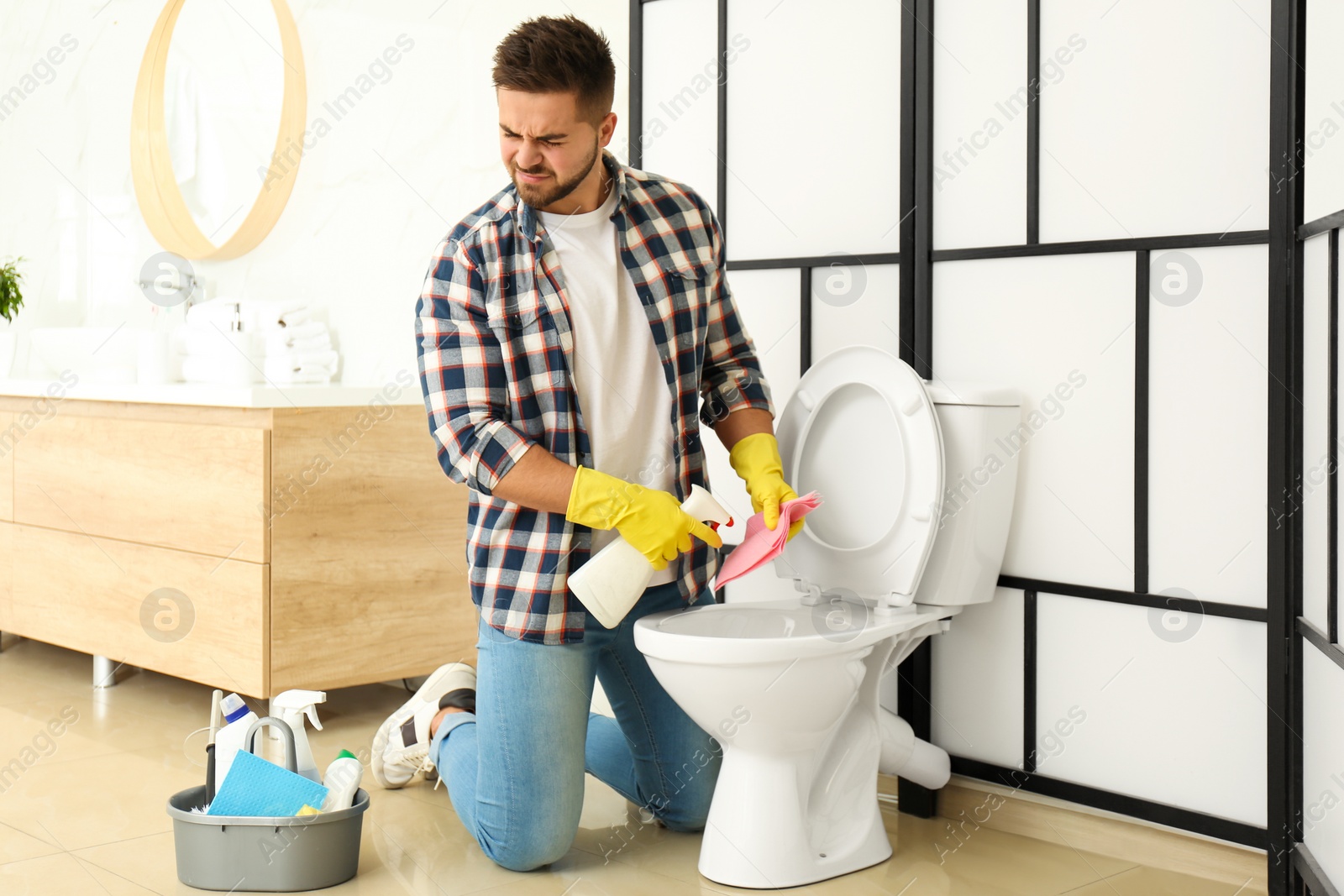 Photo of Young man feeling disgust while cleaning toilet bowl in bathroom