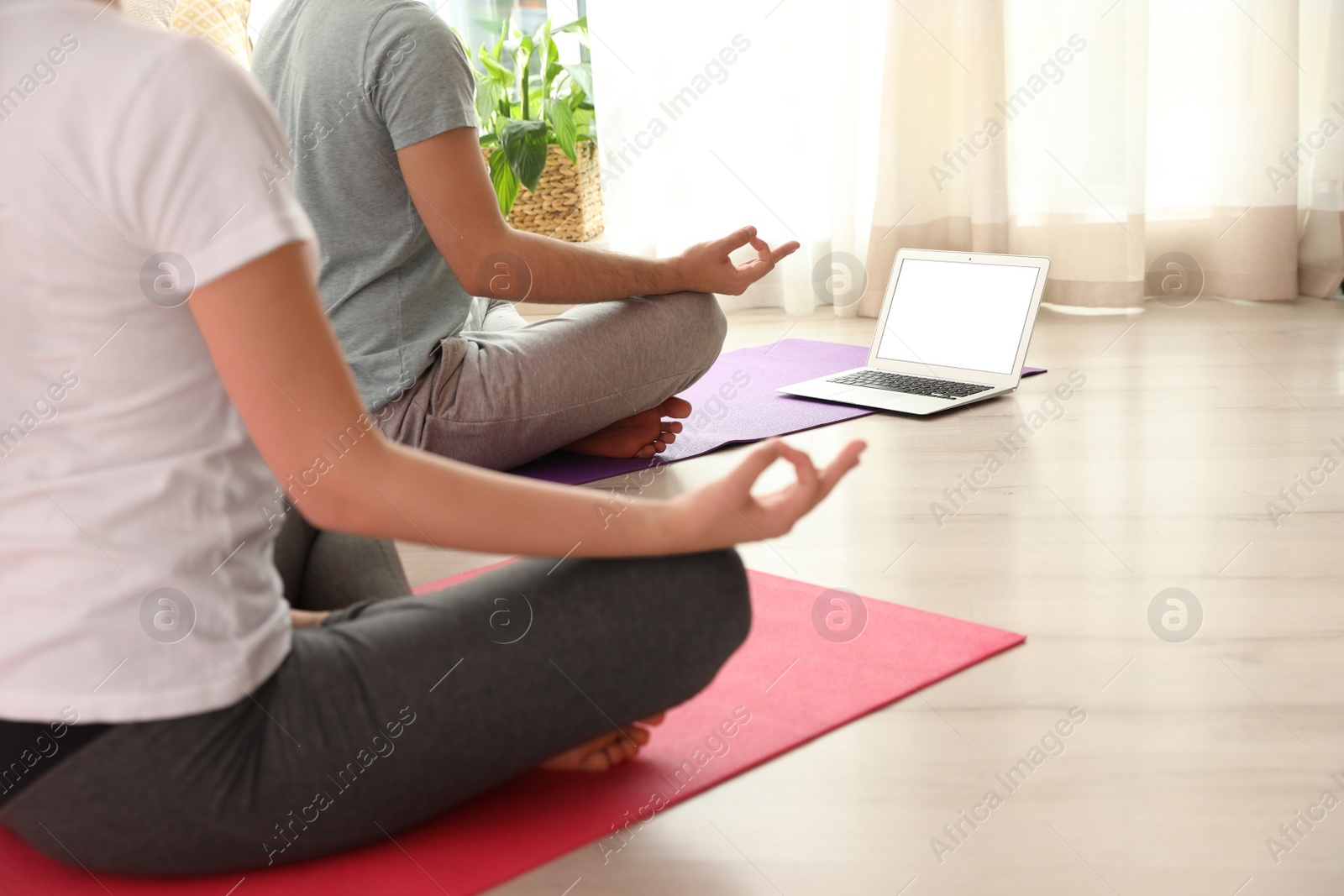 Photo of Couple practicing yoga while watching online class at home during coronavirus pandemic, closeup. Social distancing