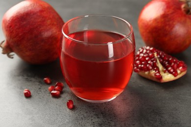 Photo of Tasty pomegranate juice in glass and fresh fruit on grey table, closeup