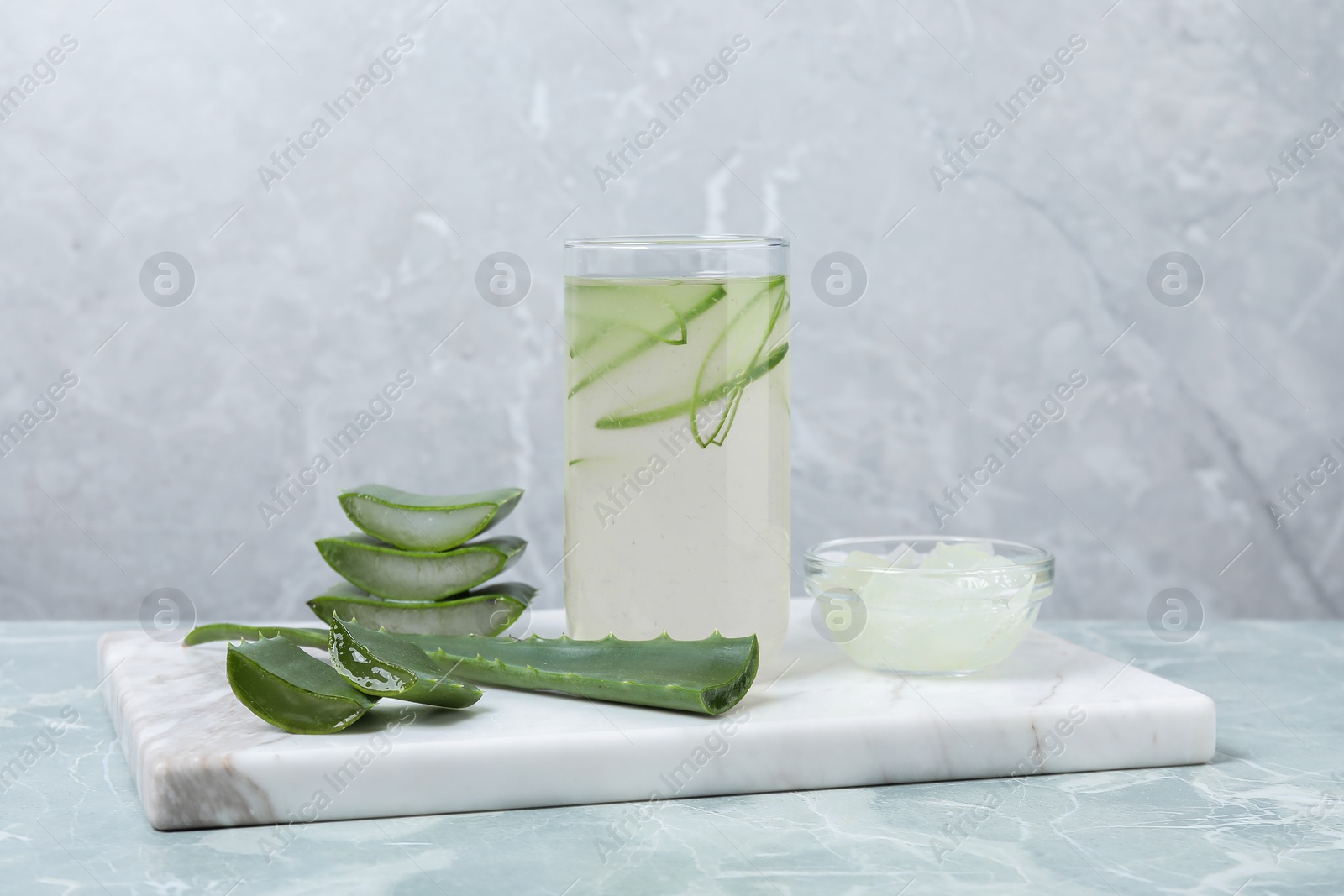 Photo of Tasty aloe juice in glass and cut fresh leaves on light grey marble table