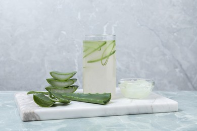 Tasty aloe juice in glass and cut fresh leaves on light grey marble table