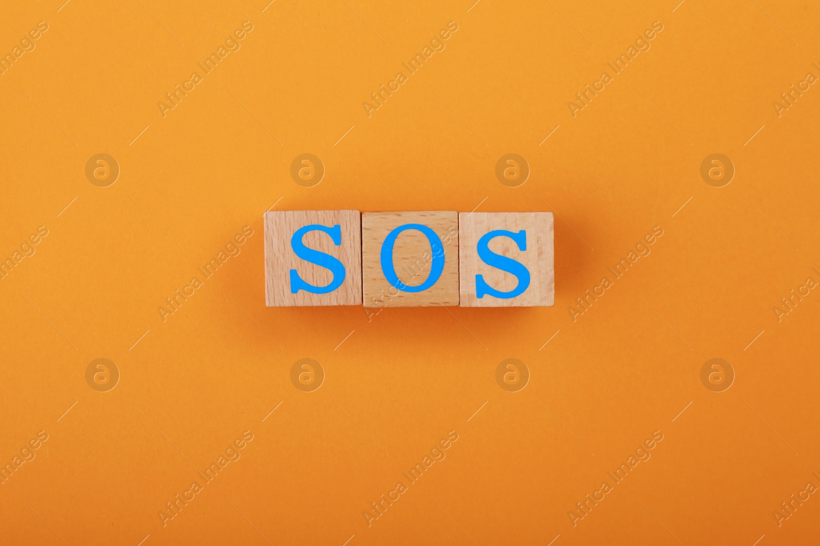 Photo of Abbreviation SOS made of wooden cubes on orange background, top view