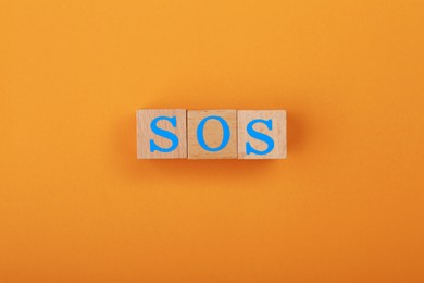 Photo of Abbreviation SOS made of wooden cubes on orange background, top view