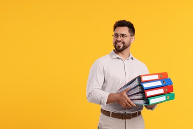 Photo of Happy man with folders on orange background, space for text