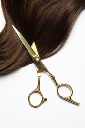 Professional hairdresser scissors with brown hair strand on white background, top view