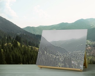 Image of Wooden easel with picture on table and beautiful mountain landscape 