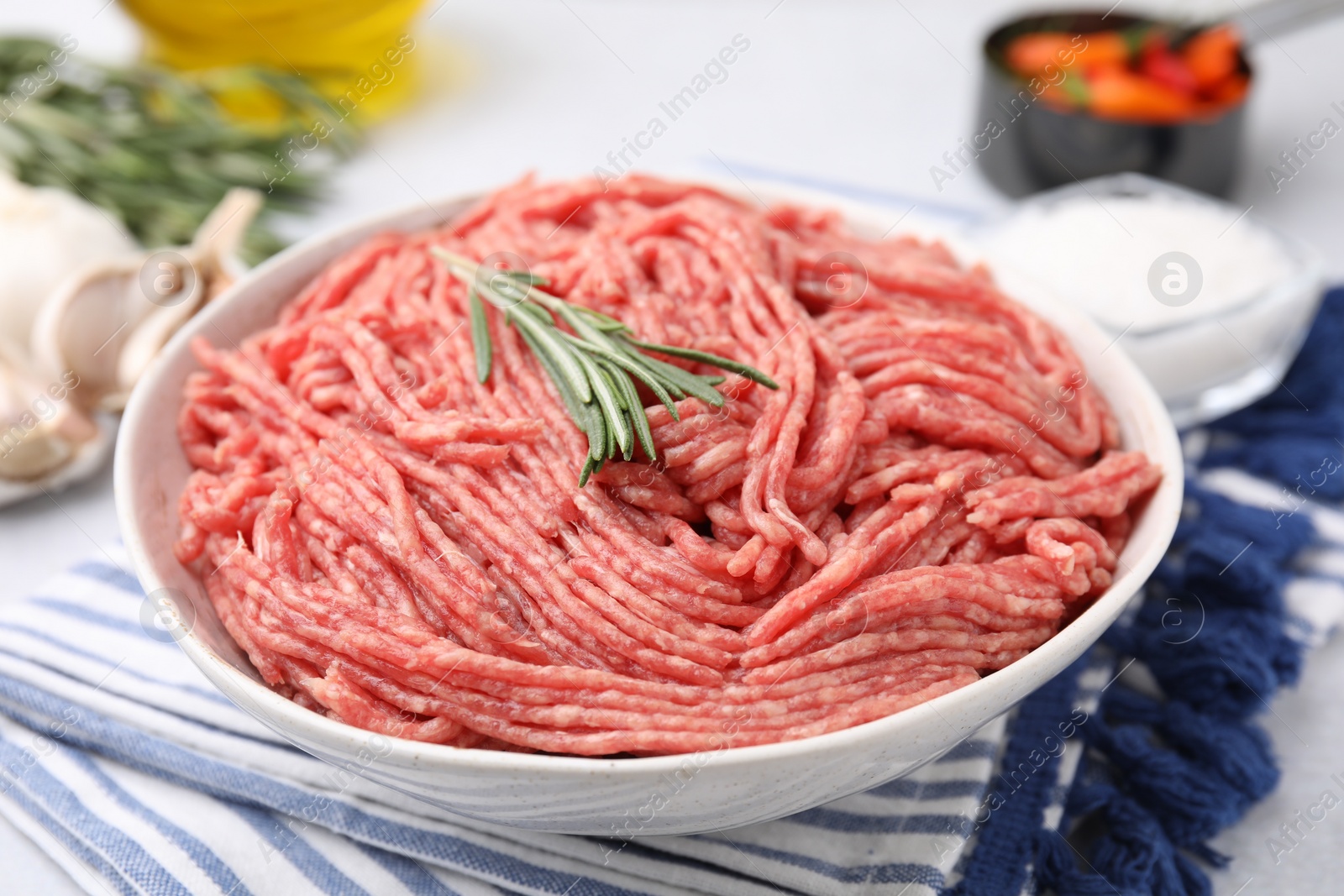 Photo of Fresh raw ground meat and rosemary in bowl on table, closeup