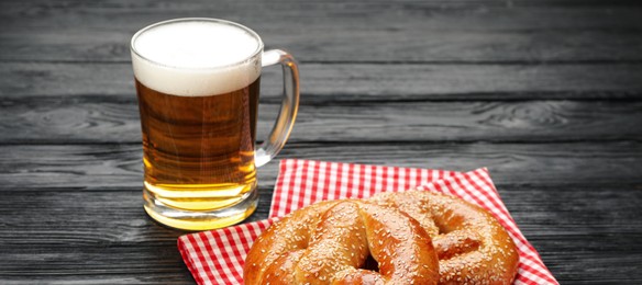 Tasty pretzels and glass of beer on black wooden table. Banner design