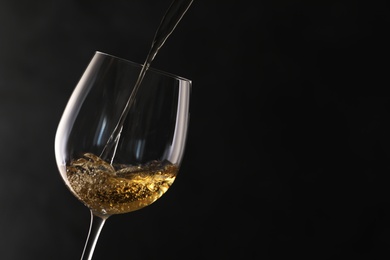 Pouring white wine into glass on dark background. Space for text