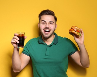 Handsome man with tasty burger and cola on color background. Space for text