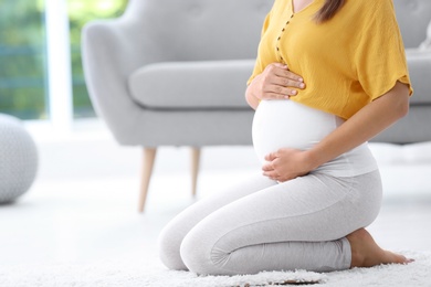 Photo of Pregnant woman sitting on floor at home, closeup