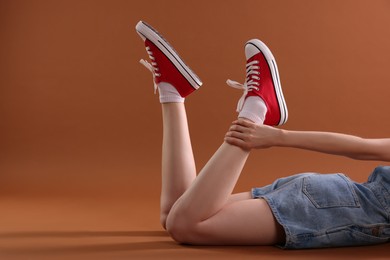 Photo of Woman wearing red classic old school sneakers on brown background, closeup. Space for text