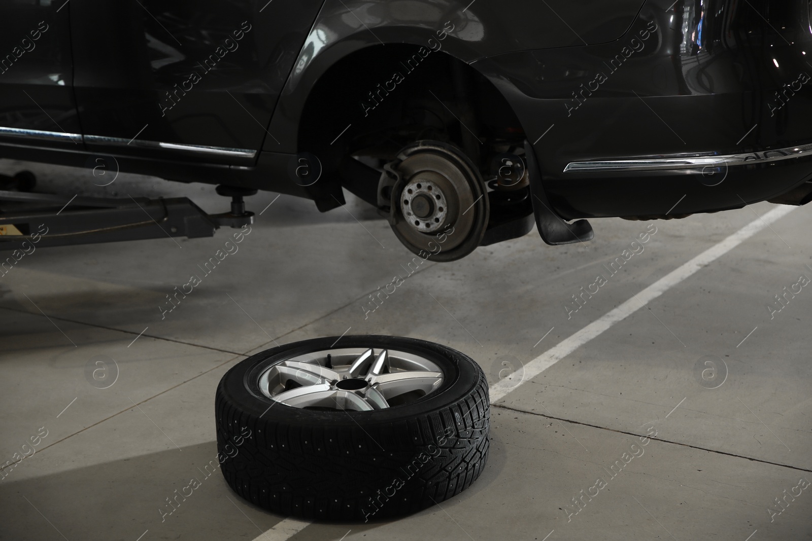 Photo of Wheel on floor near lifted car at automobile repair shop