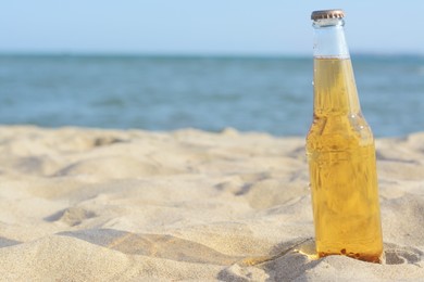 Photo of Bottle of cold beer on sandy beach near sea, space for text