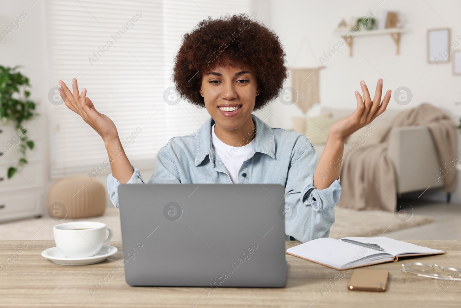 Photo of Young woman having video chat via laptop at wooden desk in room