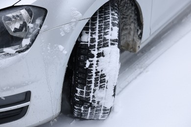 Car with winter tires on snowy road, closeup. Space for text