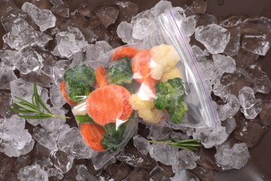 Mix of different frozen vegetables with ice on grey plate, flat lay