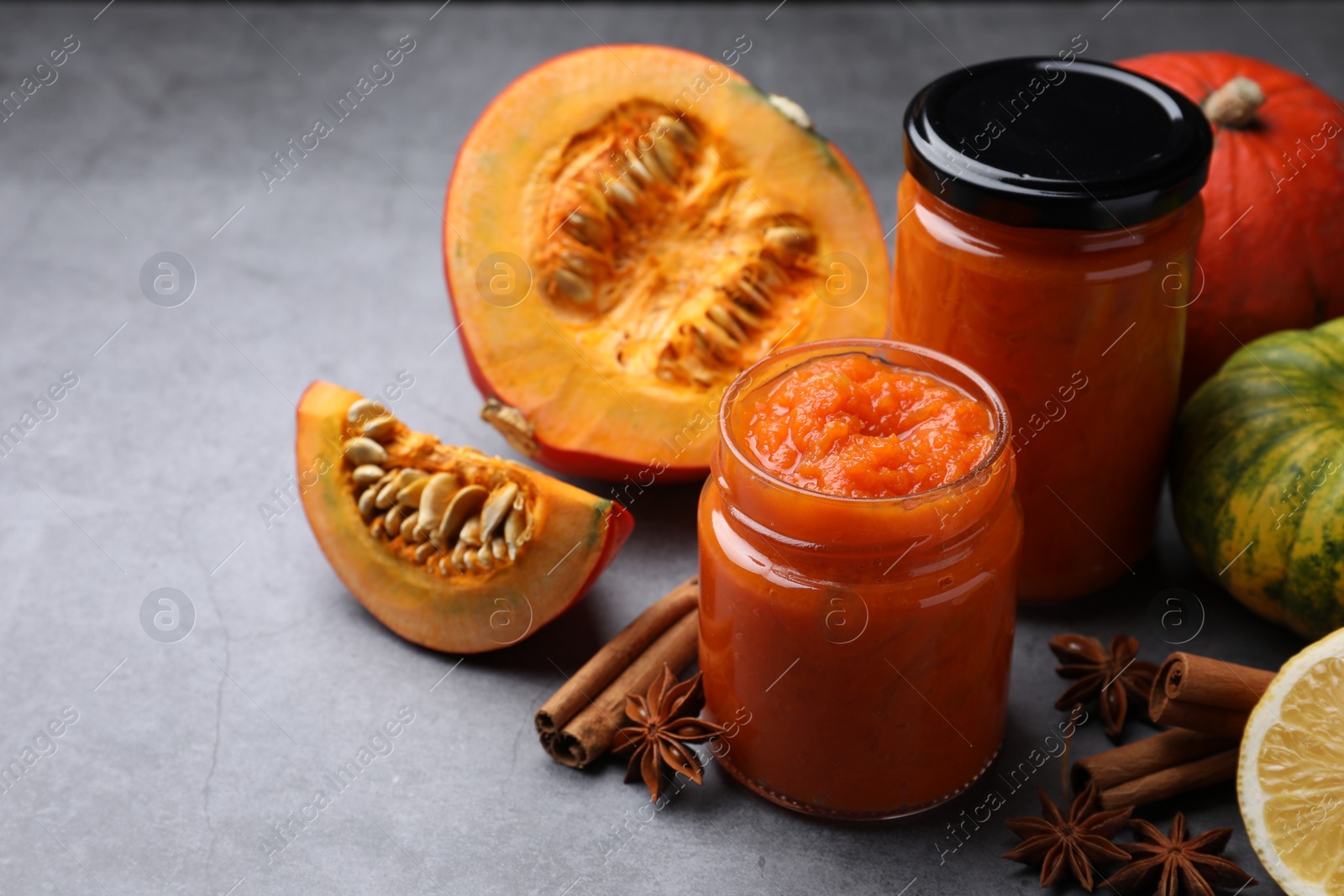 Photo of Jars of pumpkin jam and ingredients on grey table