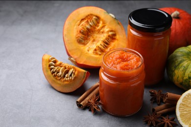 Jars of pumpkin jam and ingredients on grey table