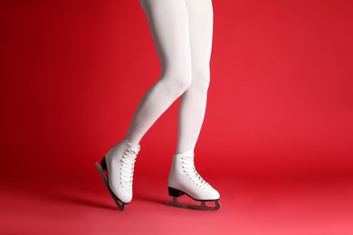 Photo of Woman in elegant white ice skates on red background, closeup of legs