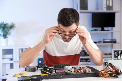 Photo of Male technician repairing motherboard at table indoors