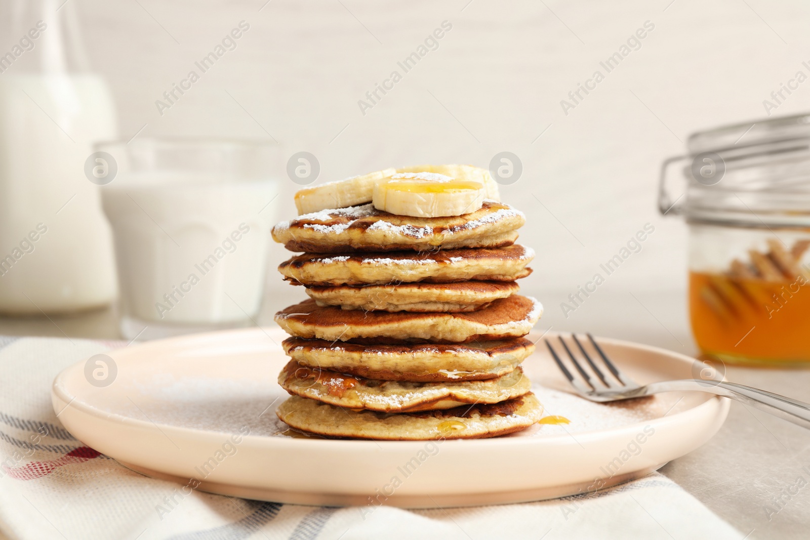 Photo of Plate of banana pancakes with honey and powdered sugar served on table, closeup