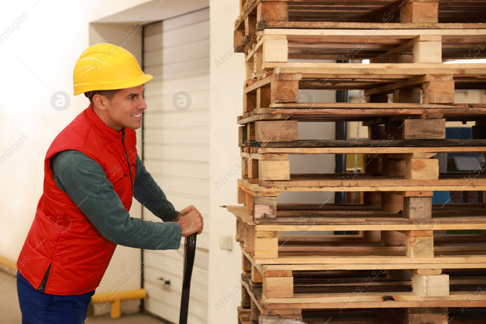 Image of Worker moving wooden pallets with manual forklift in warehouse