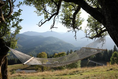 Photo of Comfortable net hammock with hat and book in mountains on sunny day