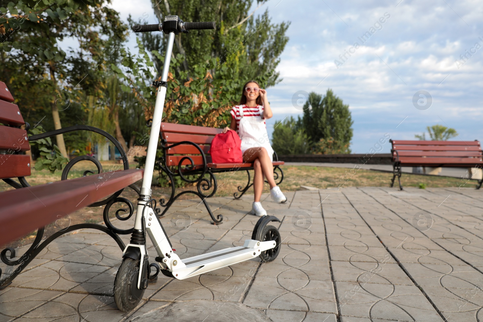 Photo of Young woman with backpack in park, focus on electric kick scooter