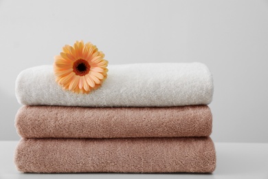 Photo of Stack of fresh towels with flower on table against white background