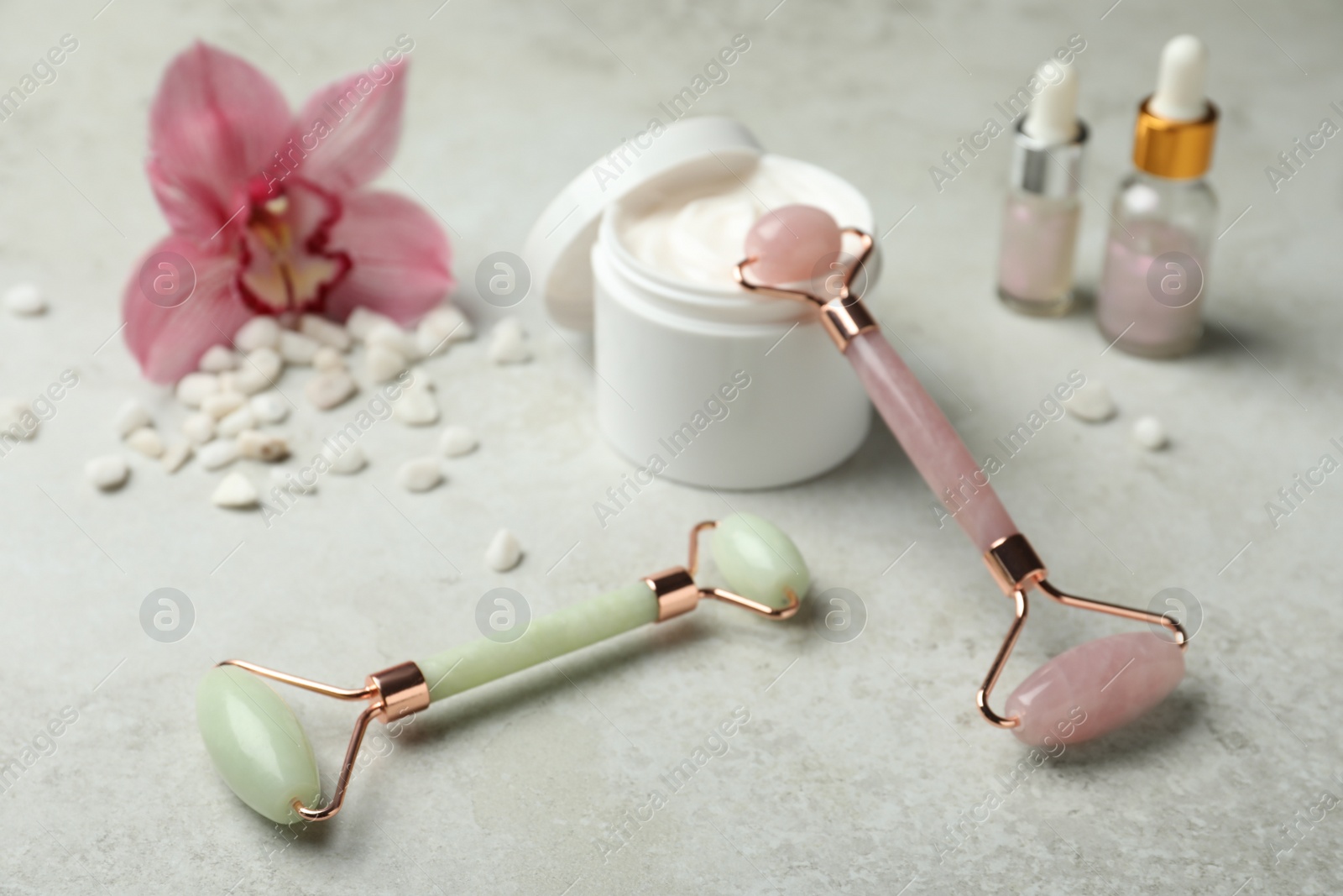 Photo of Natural jade face rollers, cosmetic products and flower on grey background