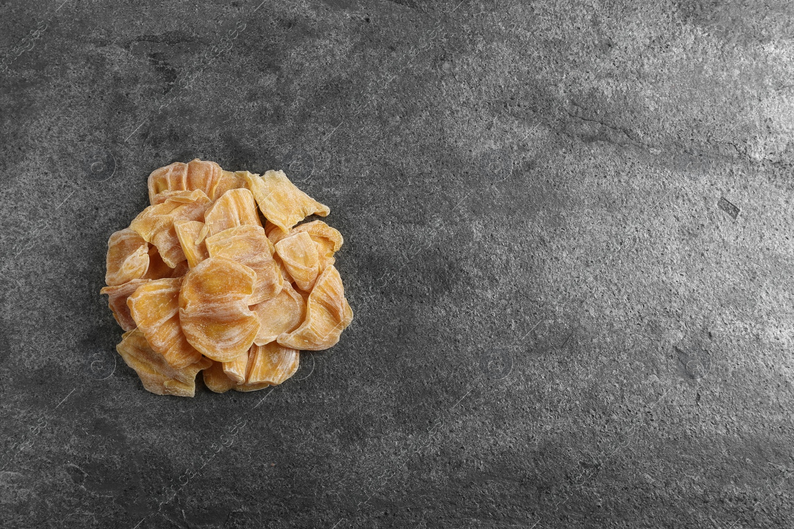 Photo of Delicious dried jackfruit slices on dark grey table, top view. Space for text