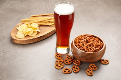 Photo of Glass of beer served with delicious pretzel crackers and other snacks on grey table