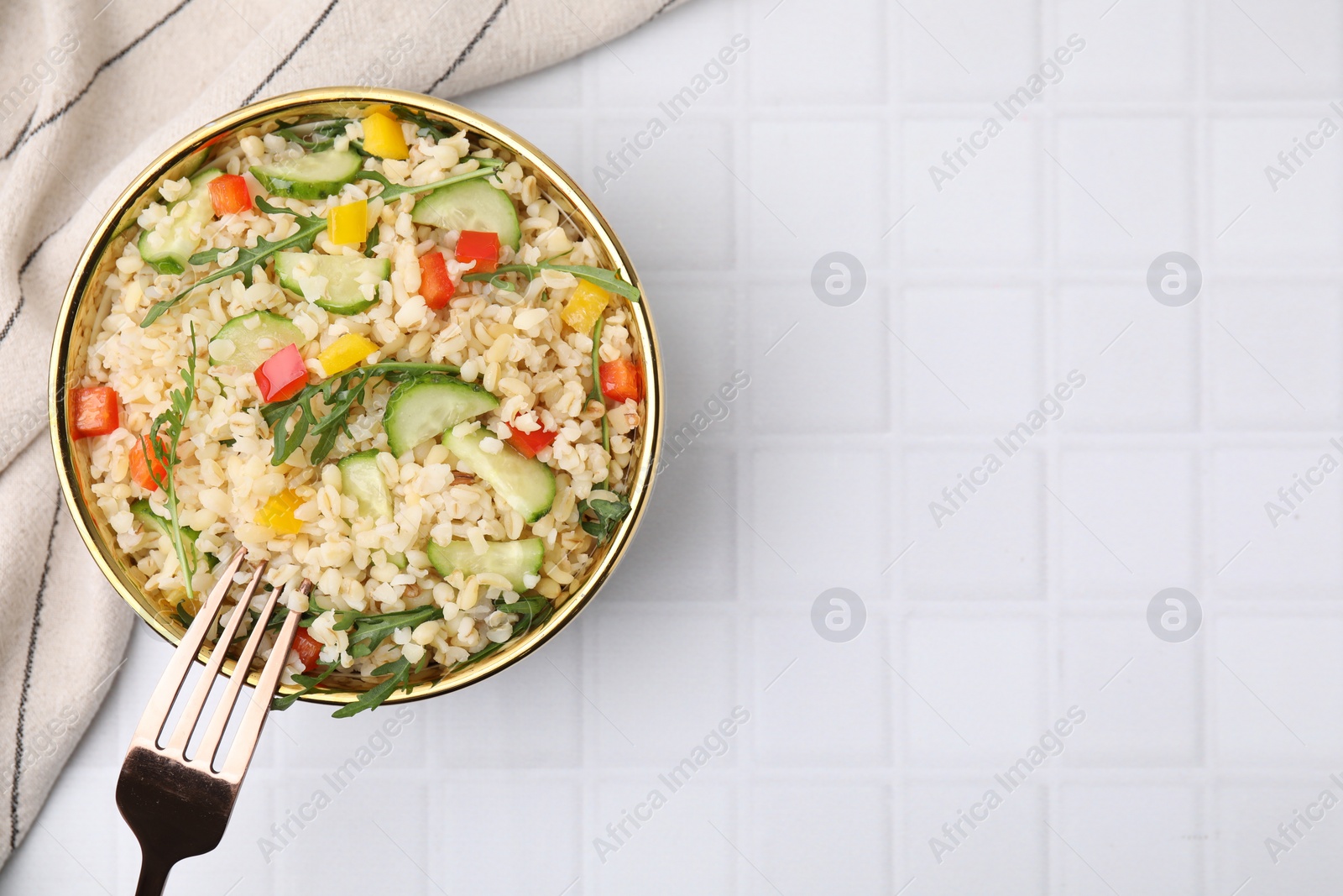 Photo of Cooked bulgur with vegetables in bowl on white tiled table, top view. Space for text