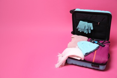 Photo of Open suitcase with warm clothes and action camera on color background, space for text. Winter vacation