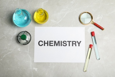 Photo of Laboratory glassware and paper with word CHEMISTRY on grey background, flat lay