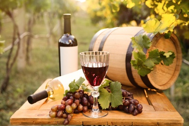 Photo of Composition with wine and ripe grapes on wooden table in vineyard