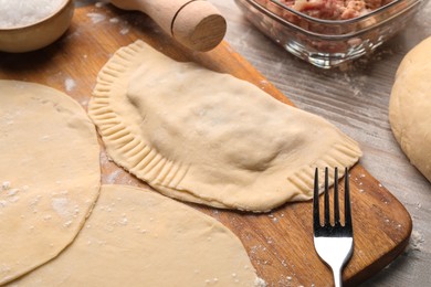 Raw chebureki with tasty filling and fork on wooden table, closeup