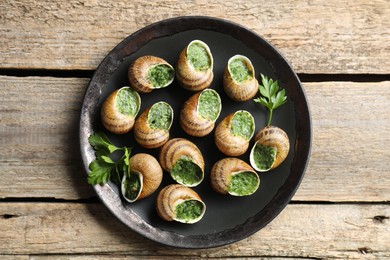 Delicious cooked snails with parsley on wooden table, top view
