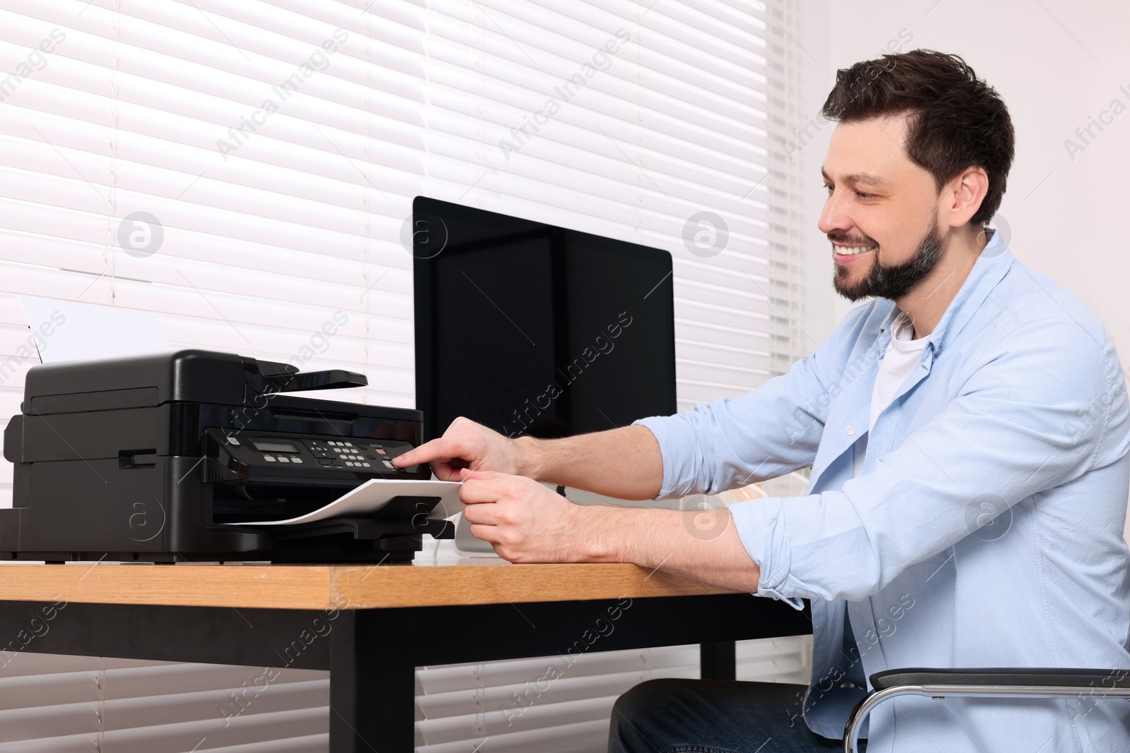 Photo of Man using modern printer at wooden table indoors