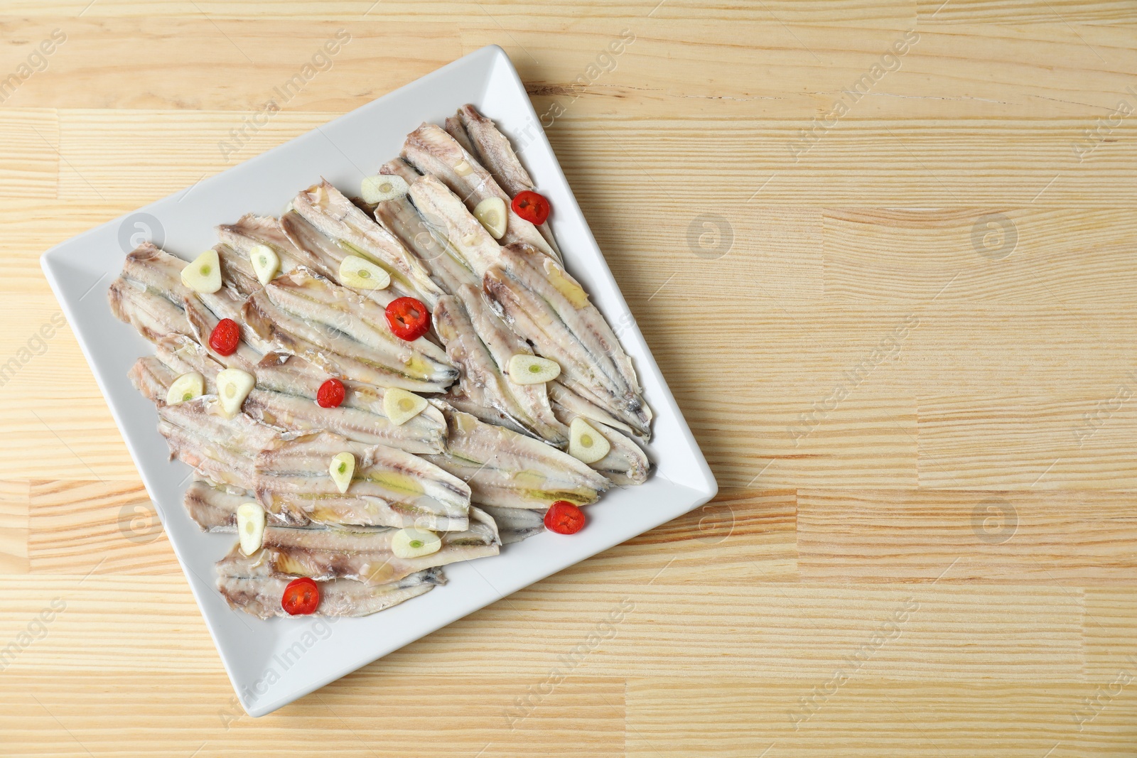 Photo of Tasty pickled anchovies with garlic and chili pepper on wooden table, top view. Space for text