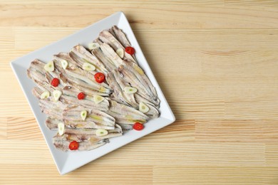 Photo of Tasty pickled anchovies with garlic and chili pepper on wooden table, top view. Space for text