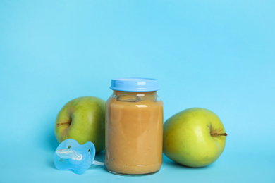 Photo of Baby food in jar, pacifier and fresh apples on light blue background