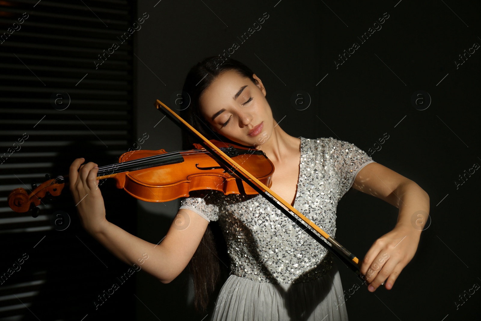 Photo of Beautiful young woman playing violin in dark room