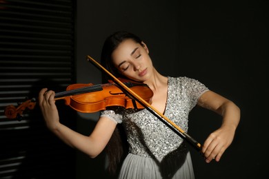 Beautiful young woman playing violin in dark room