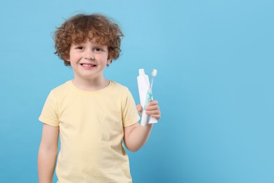 Photo of Cute little boy holding electric toothbrush and tube of toothpaste on light blue background, space for text